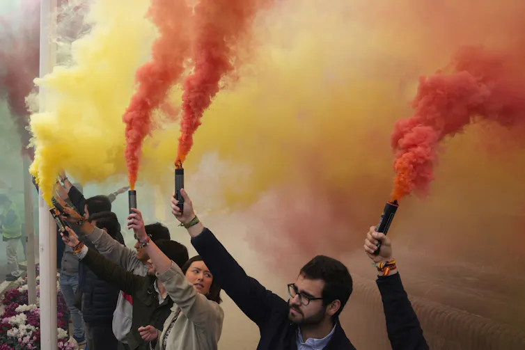 Des personnes brandissent des fusées éclairantes propulsant une fumée jaune et orange