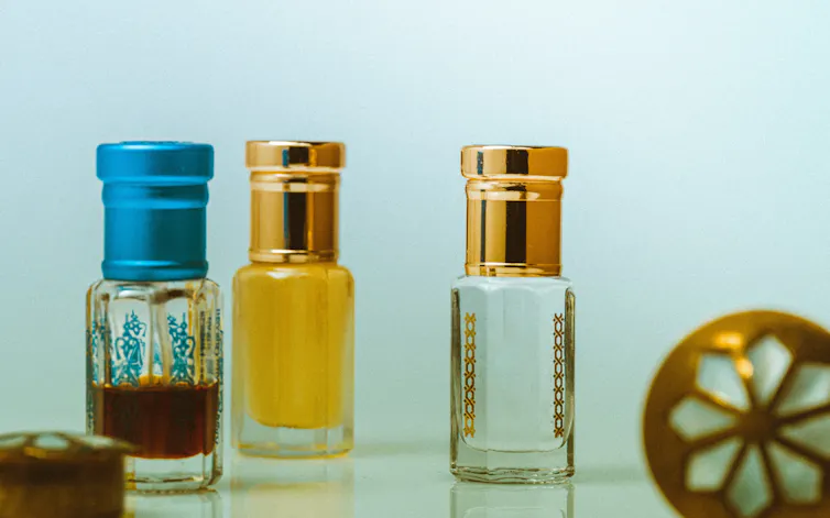 Three small perfume bottles, one is half full with a dark liquid and a blue lid, the other is full with a golden liquid with a gold lid
