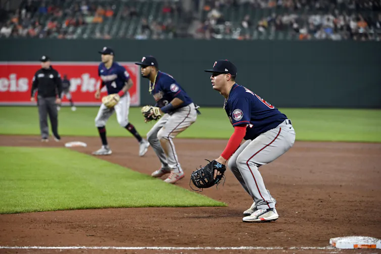 Three baseball players stand half-crouched between first and third base, presumably as they wait for the hitter to hit the ball.