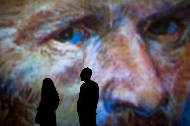 People in front of a large-scale self portrait of Vincent van Gogh.