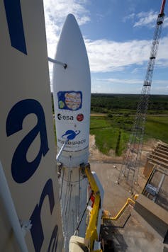 A close-up photo of a conical white rocket with ESA logo on it and a cartoon of Jupiter and Earth