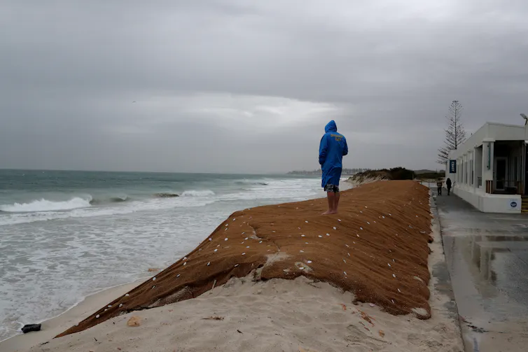 person in raincoat stands next to stormy sea