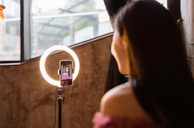 A woman looks into a smartphone attached to a ring light.