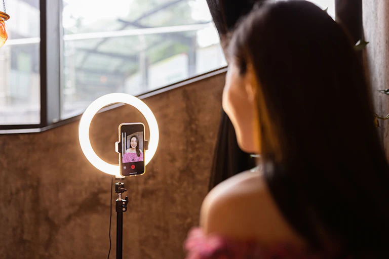 A woman looks into a smartphone attached to a ring light.
