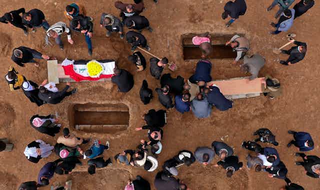 Aerial view of people around graves with two coffins in view.