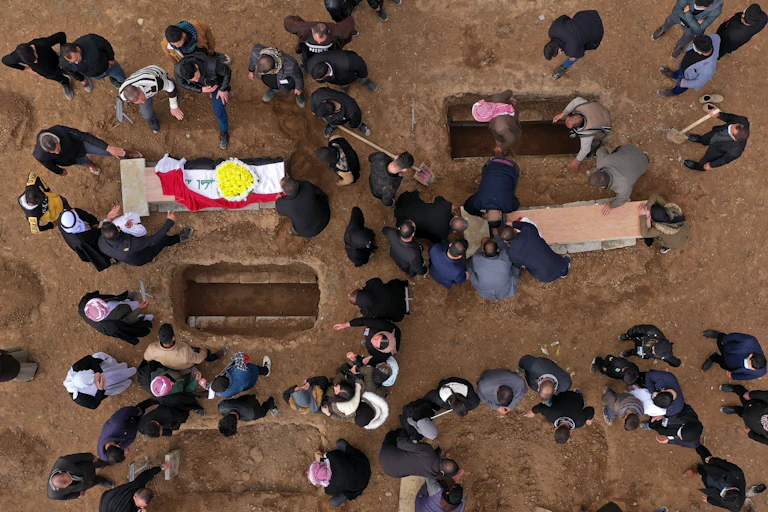Aerial view of people around graves with two coffins in view.