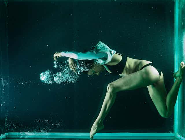 woman dancing underwater wearing a leather jacket and underwear