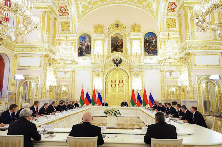 A group of men sit around a long table in an ornate room
