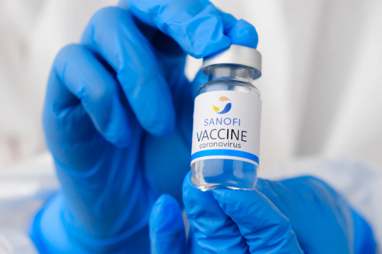 Gloved hands hold a vial of the Sanofi COVID vaccine.