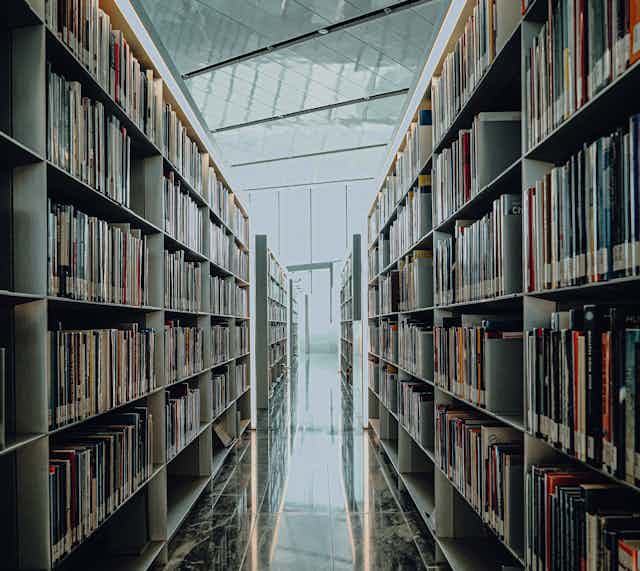 Un pasillo de biblioteca con estanterías a los lados repletas de libros.