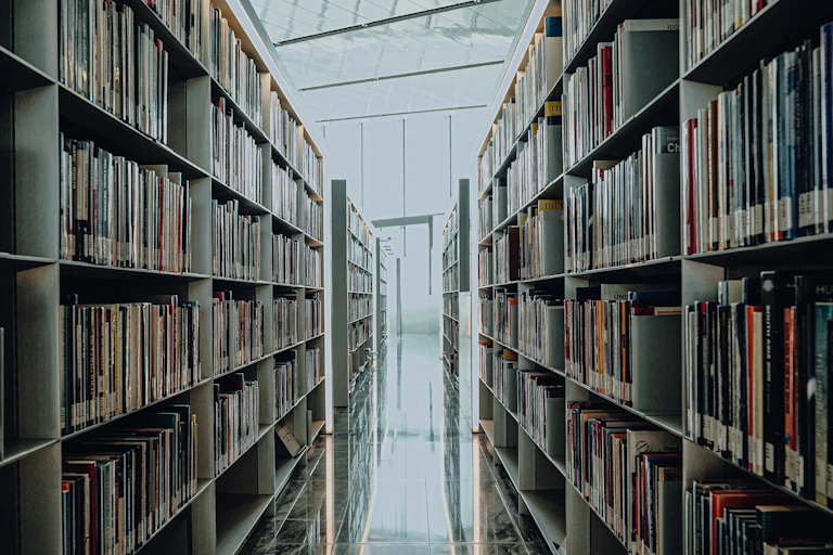 Un pasillo de biblioteca con estanterías a los lados repletas de libros.