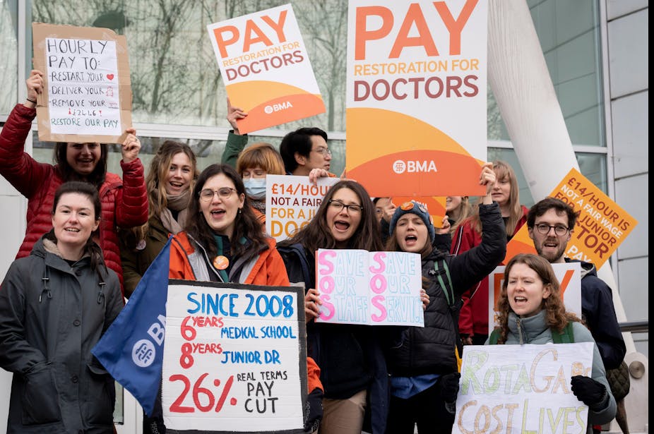 A group of striking junior doctors hold up signs demanding pay rises.