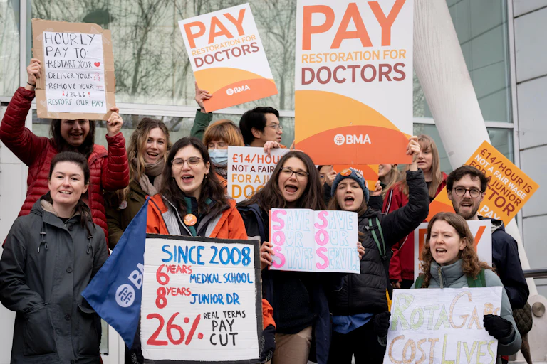 A group of striking junior doctors hold up signs demanding pay rises.
