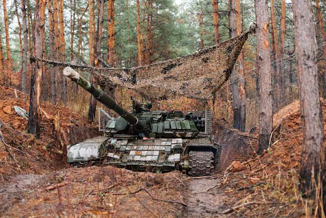 A tank with camouflage covering and surrounded by trees in the Donbas, Ukraine.