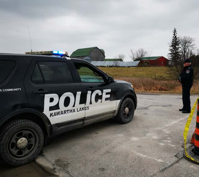 A police office stands on a rural road next to a Kawartha Lakes police cruiser.