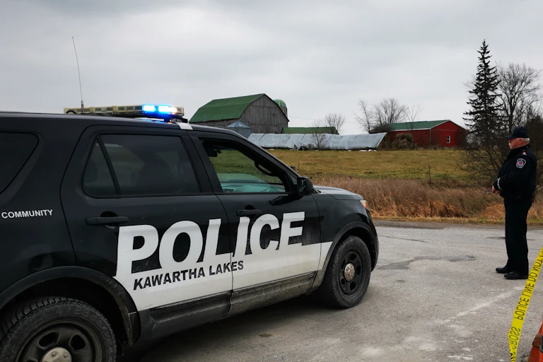 A police office stands on a rural road next to a Kawartha Lakes police cruiser.