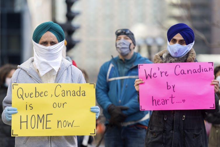 Protesters holding signs reading 'Québec, Canada is our home now' and 'We're Canadian by heart'