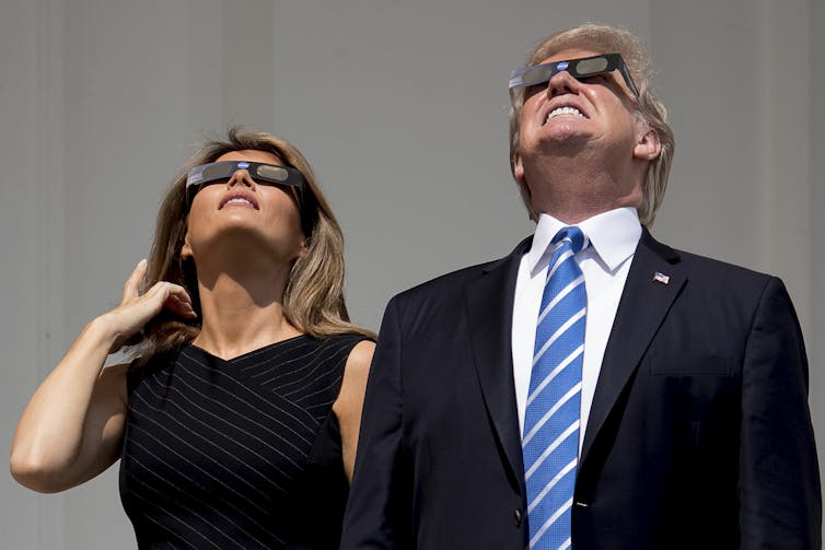 man and woman look at sun with eclipse glasses on