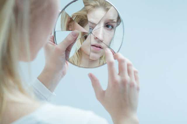 Mujer mirándose en un espejo roto.