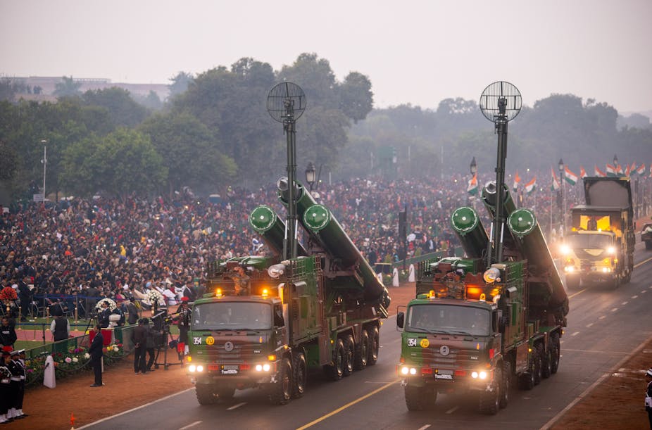 Deux camions militaires emportant des missiles sur une route, devant une foule portant des drapeaux indiens