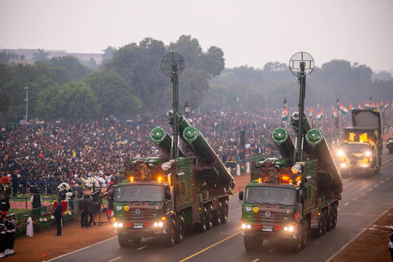 Deux camions militaires emportant des missiles sur une route, devant une foule portant des drapeaux indiens