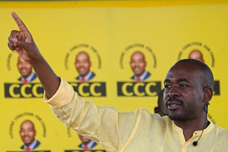 A man points ahead with his right index finger in front of banners bearing the acronym 'CCC'.