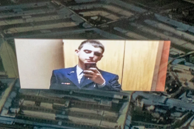 A young white man dressed in a military uniform is looking at his cellphone.
