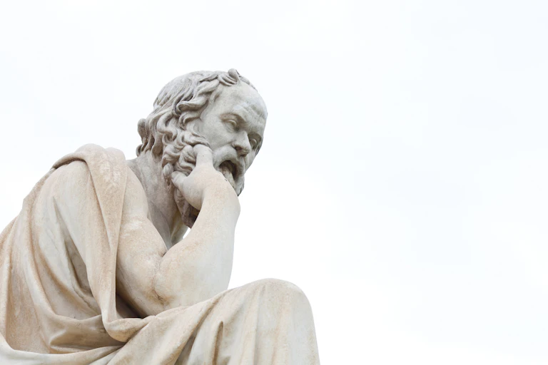 A white marble statue of a seated man with a wavy beard looking pensive.