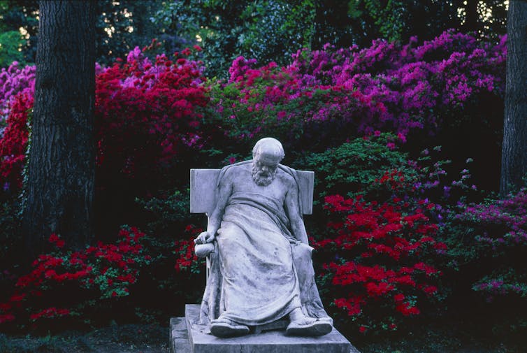 Vibrant red and purple flowers behind a statue of a slumped-over man.
