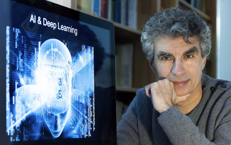 A middle-aged man with curly grey hair leans on his hand while looking into the camera. Beside him, a screen displays a visual of a human head surrounded by bright blue light with the words 'AI & Deep Learning' across the top.