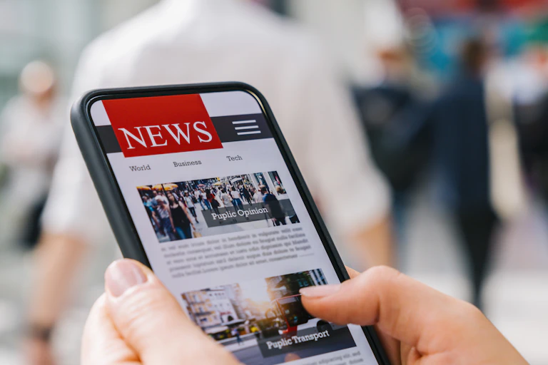 A hand scrolling through a news website feed on a cell phone