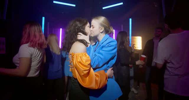 Two young women embrace and kiss in a nightclub