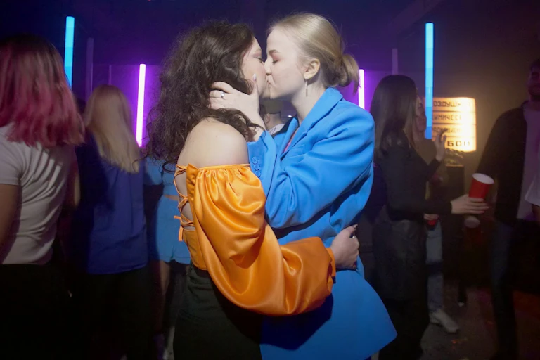 Two young women embrace and kiss in a nightclub