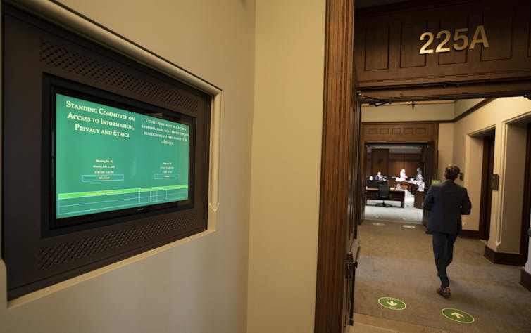 a man walks down a hallway. A green display screen shows the text Access to Information, Privacy and Ethics