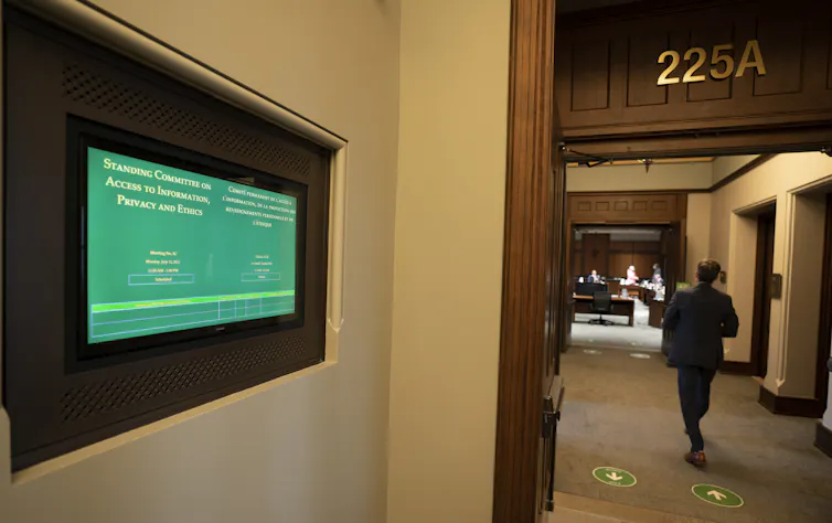 a man walks down a hallway. A green display screen shows the text Access to Information, Privacy and Ethics