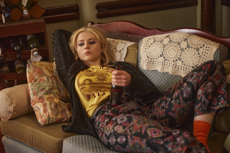 Thomasin McKenzie on the couch with a bottle of beer.