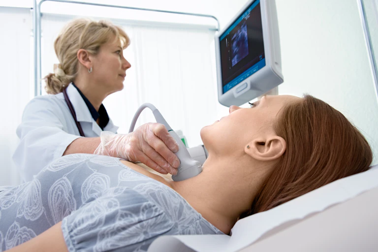 woman lying down while health worker scan her throat with ultrasound machine