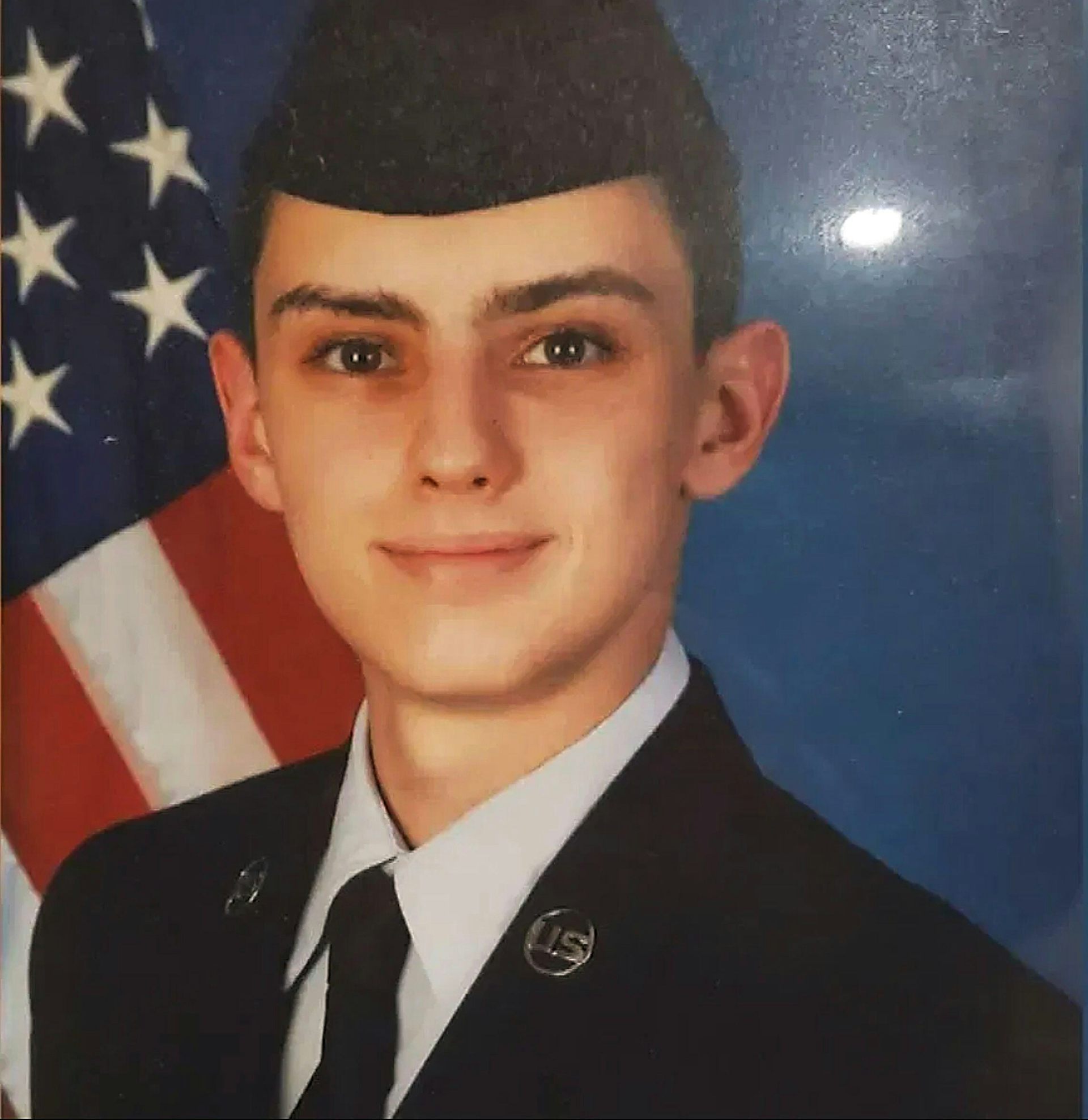 A young man in a graduation outfit in fromt of the US flag.