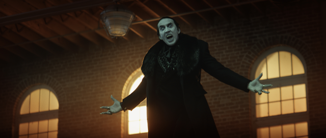 Nicolas Cage as Dracula. He's levitating in the air, arms outstretched, fangs bared. 