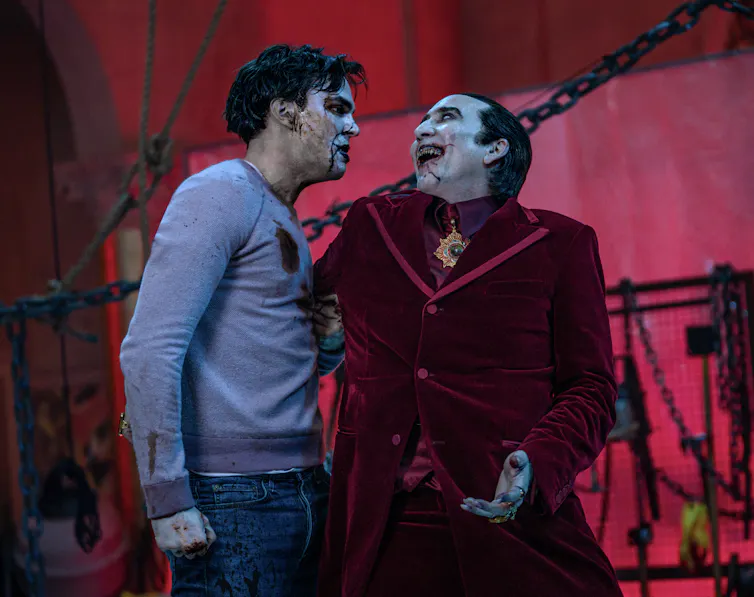 Nicolas Cage as Dracula in a red velvet cage, clutching a bloodied Nicholas Hoult as Renfield.
