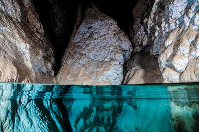 Image en gros plan de l'eau dans une grotte, avec trois gros rochers dépassant de l'eau claire.