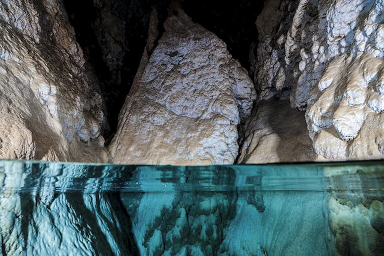 Image en gros plan de l'eau dans une grotte, avec trois gros rochers dépassant de l'eau claire.