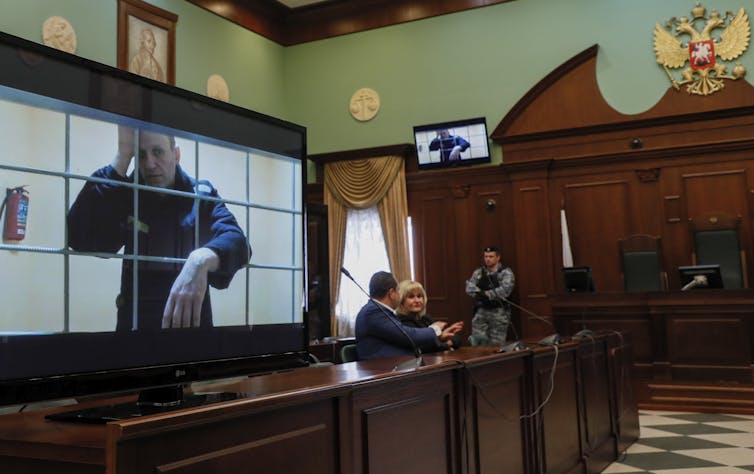 A courtroom with a television screen showing Alexei Navalny in a prison cell