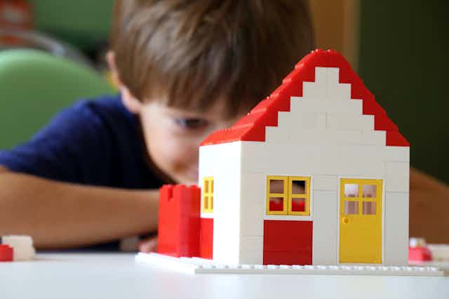 Niño tras una casita construida con bloques de construcción.