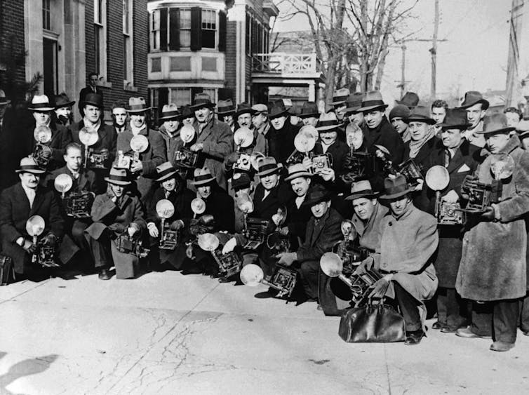 Black and white photograph of a large group of photographers posing outside a courtroom.