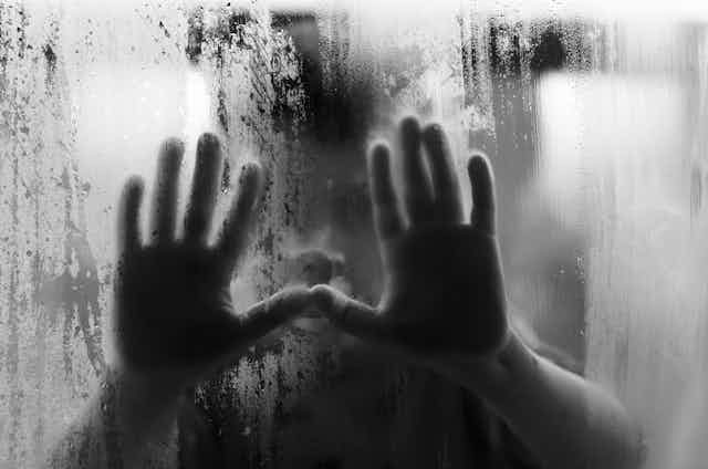 black and white image of a child's hands up against a rainy, misty window