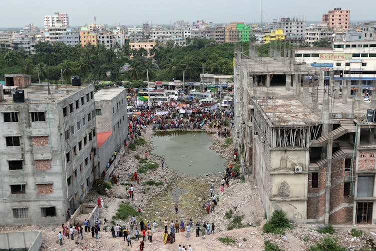 A large hole between two buildings, with a crowd of people stood around it
