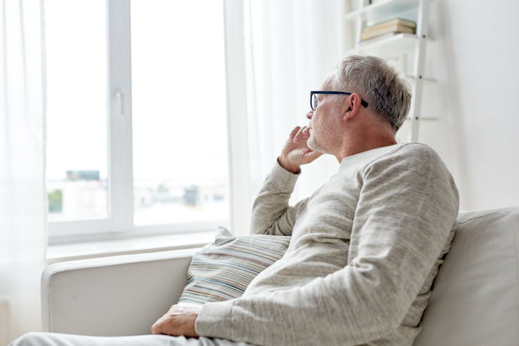 A middle aged man sitting on a couch and looking solemnly out a window