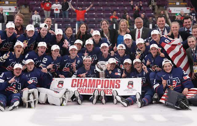 A group of women in blue hockey kits pose for a photo with a trophy and a banner that reads: champions