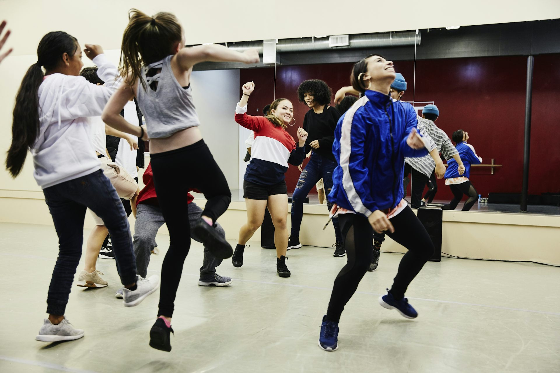 A group of hip-hop dancers, in sweats and stockings, practice in a dance studio.